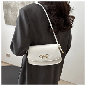 Detailed view of the white flap shoulder bag featuring a gold bow metallic buckle
