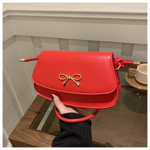 Detail of red crossbody bag featuring a golden bow ornament and knot strap detail