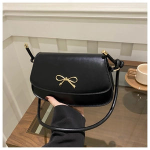 Detail of a black leather crossbody bag featuring a elegant gold bow metal buckle