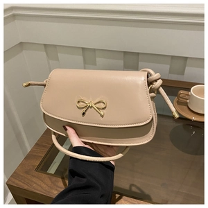 Close-up of cream crossbody bag featuring a golden bow buckle and knotted strap detail