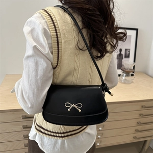 Minimalist black leather half-moon shoulder bag with a gold bow buckle on a model