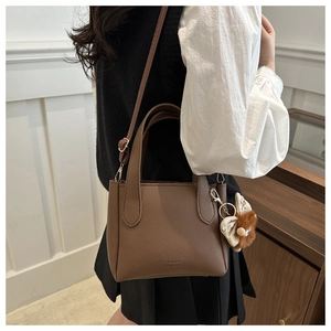 Detail of dark brown lychee leather bucket bag with plush charm and fashion typography