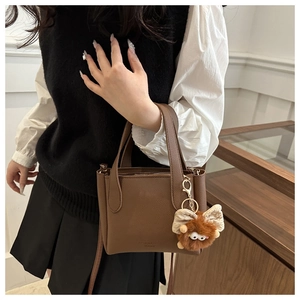 Detail of a brown lychee pattern leather bucket bag with a plush monster charm