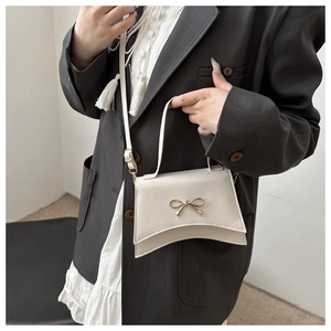 Sac nœud crème élégant porté avec un blazer gris et une chemise à franges blanche