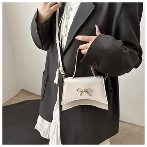Détail du sac bandoulière crème avec boucle nœud doré et fond asymétrique sur modèle