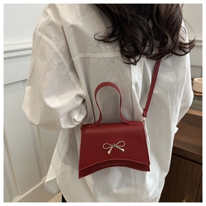 Détail du sac bandoulière en cuir rouge mat avec boucle nœud doré sur le modèle