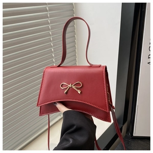 Détail d'un sac à bandoulière rouge avec nœud en métal doré et poignée élégante