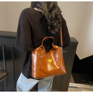 Detail view of the vintage brown leather handbag with a triangle metal emblem and strap