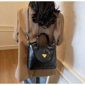 Close-up of black glossy leather bucket bag with a golden triangular metal emblem