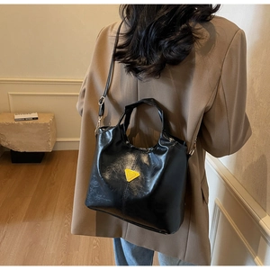 Detail of black glossy bucket bag with yellow triangle logo shown on model shoulder