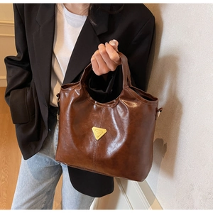 Detailed view of brown oil-wax leather tote bag with gold triangle plaque and twin handles