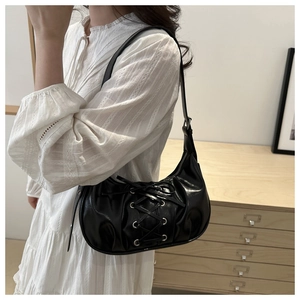 Detail of crossbody bag with lace-up bow design and glossy black faux leather texture