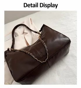 Detail shot of a dark brown PU leather tote bag with a metal chain on a white blazer