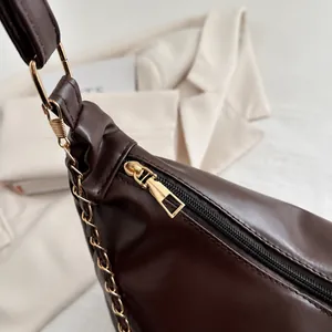 Detail of smooth gold metal zipper and leather chain strap on dark brown tote bag