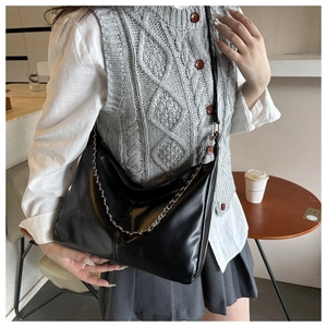 Detail of black leather crossbody bag with decorative metal chain on grey knit vest