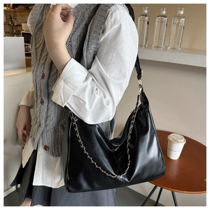 Detail of a black glossy PU leather shoulder bag with a delicate gold chain decoration