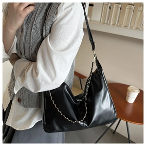 Detail of black faux leather tote bag featuring a gold chain and adjustable shoulder strap