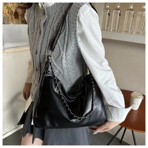 Detail shot of black faux leather tote with decorative metal chain and soft glossy finish