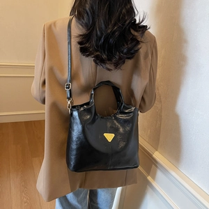 Glossy black bucket bag with gold triangle detail shown from back view on model