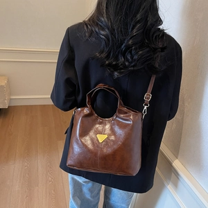 Brown vintage leather bucket bag with metallic triangle logo shown on a model