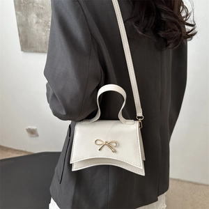 Petit sac blanc à nœud doré avec base incurvée porté en bandoulière par un mannequin