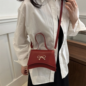 Petit sac bandoulière rouge avec nœud doré porté par un mannequin en style printemps