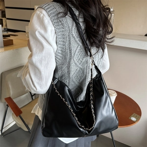Chic black PU leather hobo tote bag with gold metal chain on a casual model outfit