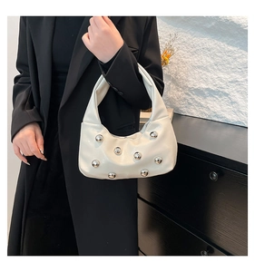 Détail du sac à main crème avec rivets métalliques argentés sur cuir brillant et anse unique