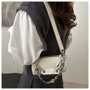 Close-up of cream cylindrical crossbody bag with bold silver chain and leather strap