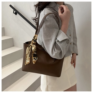 Detail of dark brown leather tote bag with elegant silk scarf tied on the handle