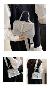 Detail of grey crossbody bag with crocodile texture, metal buckle, and wide woven strap