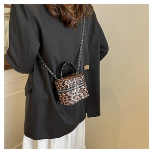 Detail of leopard print cylinder bucket bag with chain strap and top handle on model