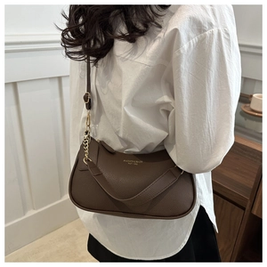 Macro detail of dark brown litchi grain leather texture and gold chain strap on shoulder bag