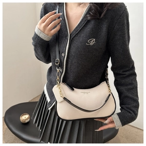 Model wearing a chic beige crescent underarm bag with black trim and gold chain detail
