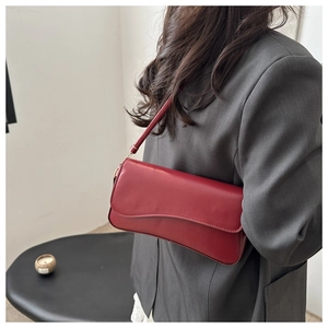 Detail of burgundy leather underarm bag with curved flap and wide shoulder strap