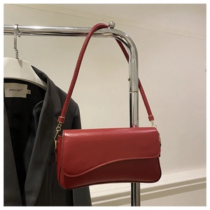 Detail view of red leather underarm bag with asymmetric flap and golden metal buckles