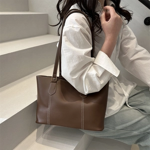 Brown leather tote bag with contrast stitching and shoulder straps in a minimalist design
