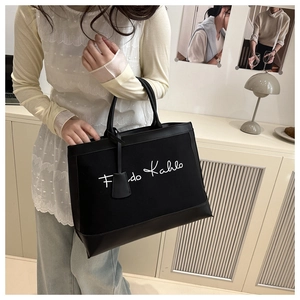 Close-up of black canvas tote bag with white Frida Kahlo script and leather details