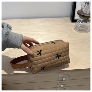 Close-up of khaki quilted clutch bag featuring black bow embroidery and fabric handle