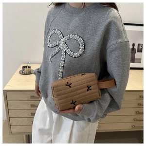 Close-up of quilted beige clutch with black embroidered bows and side handle strap