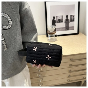 Detail of black quilted clutch with pink bow embroidery and convenient side handle