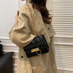 Modern black quilted crossbody bag with gold chain strap shown on khaki trench coat