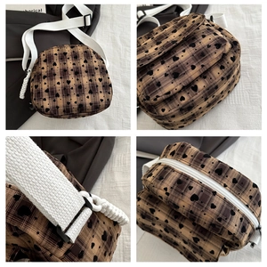 Detail view of brown checkered crossbody bag with black heart patterns and white woven strap