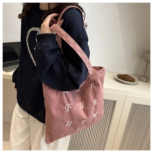 Détail du sac cabas en velours côtelé rose avec broderie porté par un mannequin en intérieur