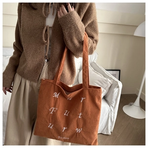 Detailed close-up of orange corduroy tote bag featuring white letter embroidery and texture