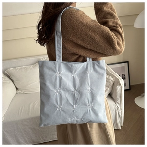 Detail of light blue corduroy tote bag showing embroidered letters and soft texture