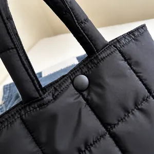 Detail shot of black quilted tote bag showing snap button closure and nylon fabric texture