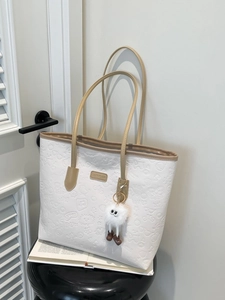 Sac cabas blanc minimaliste avec motifs floraux gaufrés et breloque peluche sur un siège
