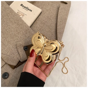 Exquisite goldene Schmetterlings-Clutch mit Metallkette vor einem Tweed-Blazer