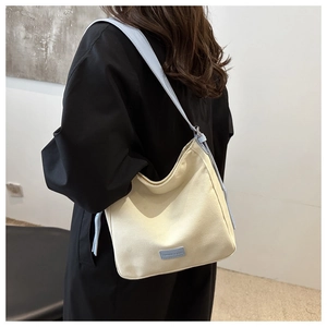 Détail du sac fourre-tout en toile crème avec bandoulières en cuir bleu clair et plaque